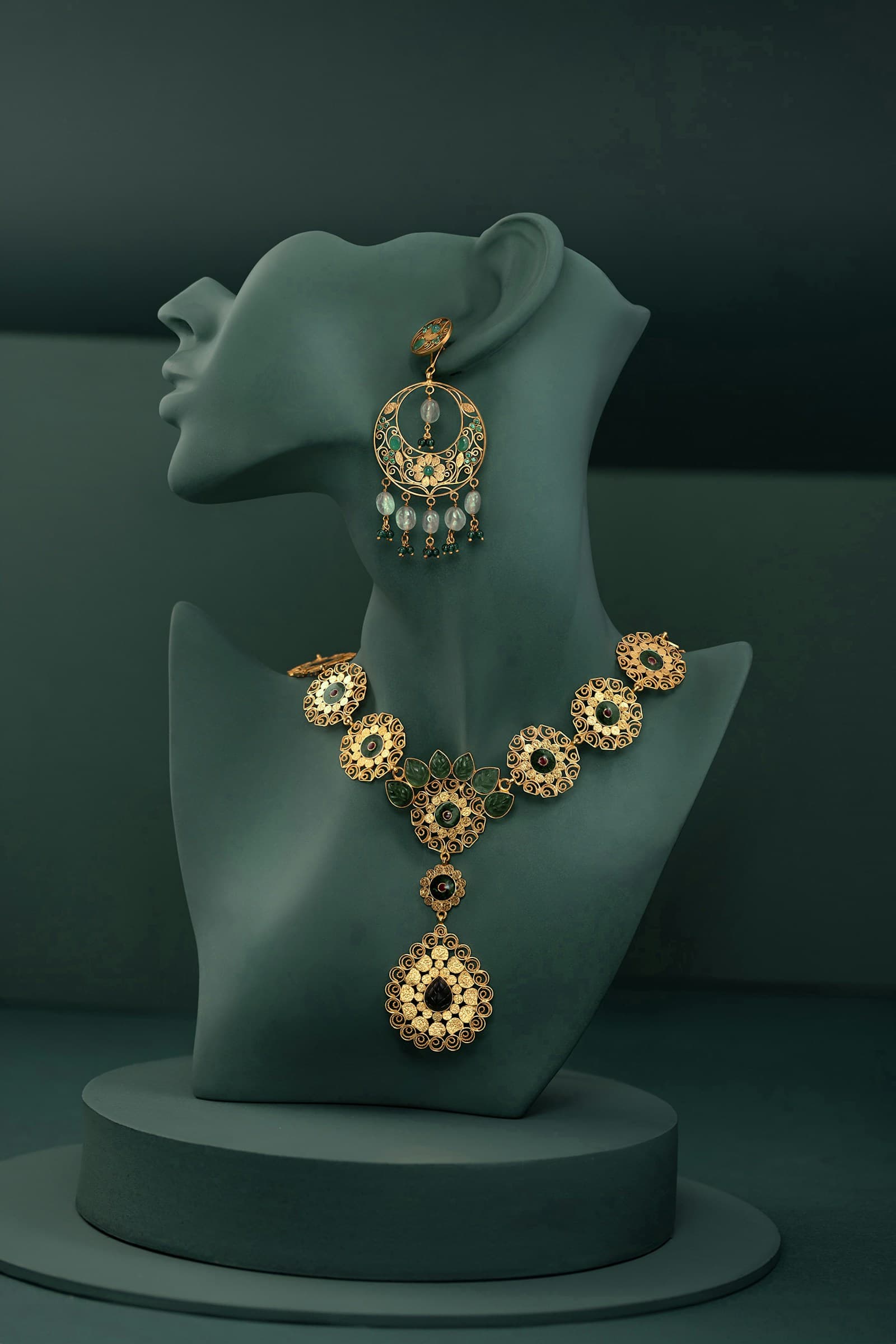 Traditional gold necklace and earring set displayed on dark green